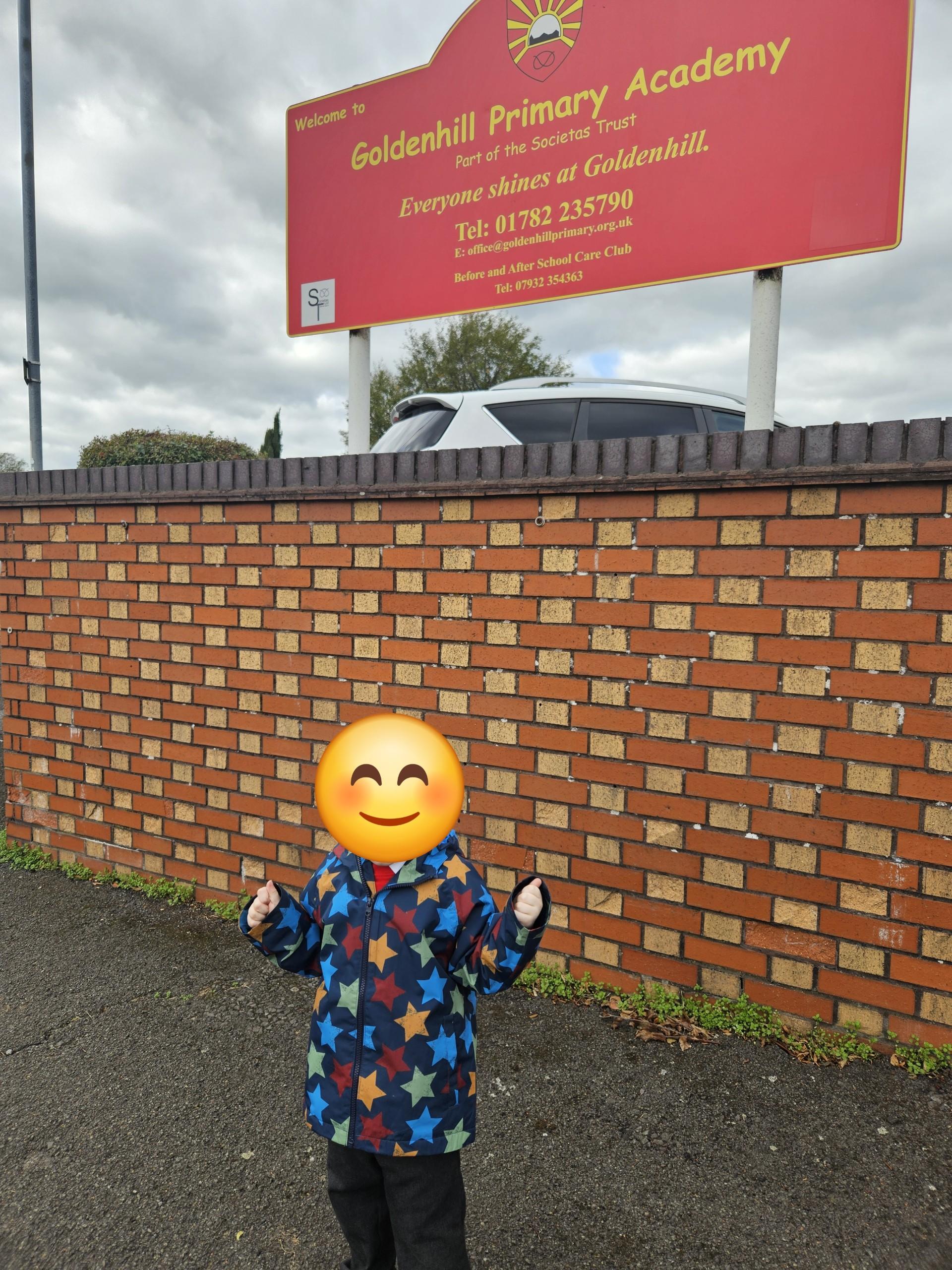 Picture of a young child with arms outstretched to the side in front of the Goldenhill Primary Academy sign.